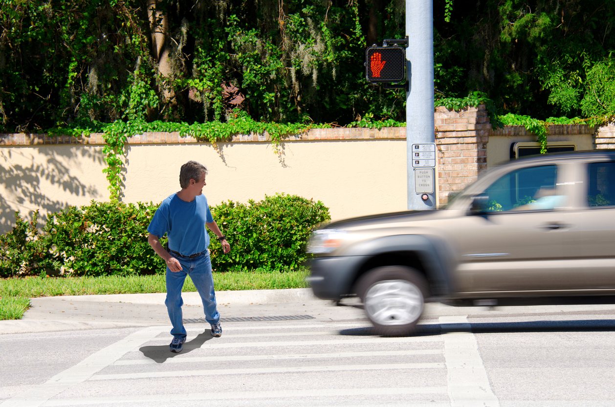 A man in a pedestrian crosswalk almost hit by a vehicle speeding through the crosswalk.